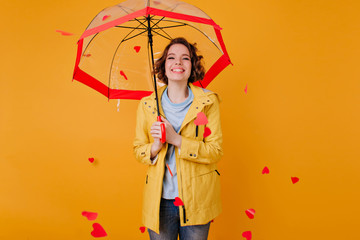 Blissful pale girl in stylish jacket standing under parasol with sincere smile. Young woman in elegant autumn attire posing on yellow background. © Look!