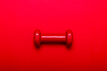 Red dumbbell for fitness isolated on dark red background.