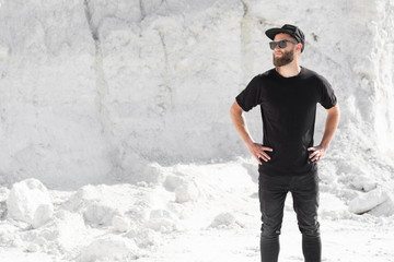 Hipster handsome male model with beard wearing black blank t-shirt and a baseball cap with space...