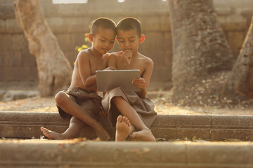 Two Asian boys are interested in learning different things on their tablets. The concept of distance education via the internet © boonchok