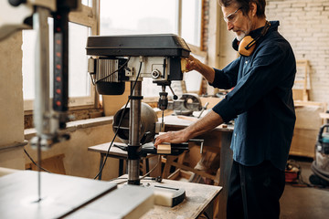 Carpenter drilling wood on machine. Male carpenter working in his workshop. 