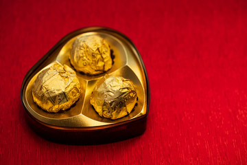 Chocolate Day Gift Box. Heart shape golden luxury chocolate box isolated on red background with copy space. Valentine day gift concept for poster, banner, graphic resources, magazine, invitation card.