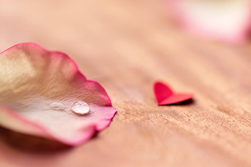 Pink Petal Romantic Wallpaper. Beautiful droplet on a pink rose petal with a cute little red heart on wooden table with copy space for Valentines day, wedding, anniversary. 