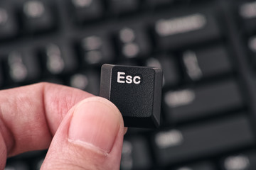 Man's hand holding Escape key against black keyboard