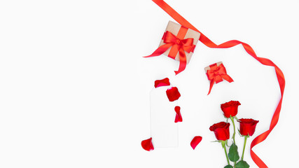 Red roses, silver blank mockup, red ribbon, craft paper gift, petals isolated on white backdrop. Copy space. Romantic festive template concept for greeting card, advertising, Women’s day, Mother's Day