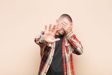 young handsome man covering face with hand and putting other hand up front to stop camera, refusing...