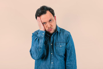Young man with expression of extreme tiredness and sadness. Denim shirt and isolated pink...