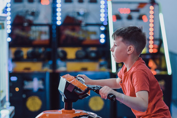 Indoor activity. European boy in red t-shirt playing racing simulator in play ground in shopping mall. He is enjoying his leisure time. - 320838258