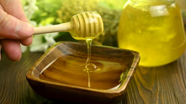 male hand stirs honey with a wooden spoon