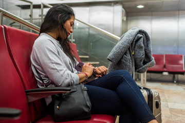 Fototapeta na wymiar Latin girl watches the time on her smartwatch waiting for her flight to arrive in the airport waiting room