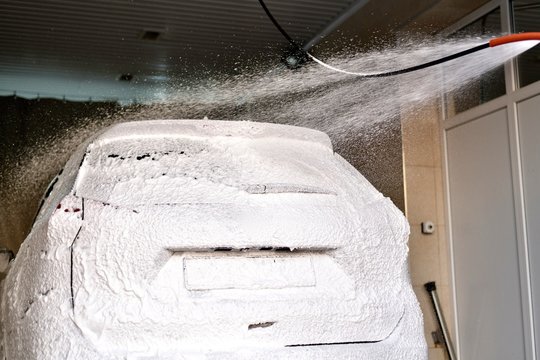 The Car Is All In White Foam Under A Spray Jet On Top Of The Car Wash.