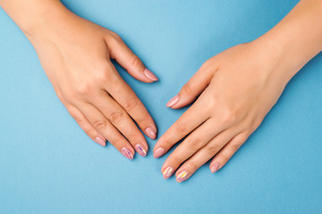 Female hands with tender manicure on a blue background, top view. Skin care concept