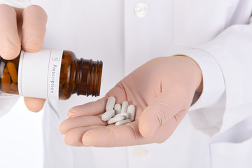 Closeup of a doctor pouring pills into his gloved hand.