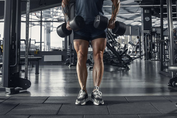 Confident. Young muscular caucasian athlete practicing in gym with the weights. Male model doing strength exercises, training his upper body. Wellness, healthy lifestyle, bodybuilding concept.