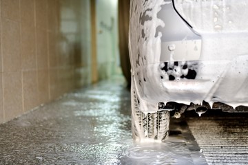 The car in soap foam, a fragment of the rear bumper and wheel, stands wraps on the soapy surface...