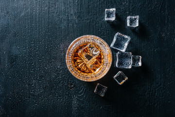 glass of whiskey with ice on a wooden table surrounded by smoke