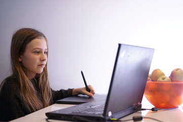 girl at home learns to draw on the laptop using a tablet and pen
