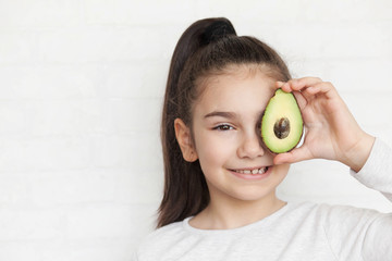 Happy child girl with avocado. Healthy lifestyle. Real emotions. Fun.