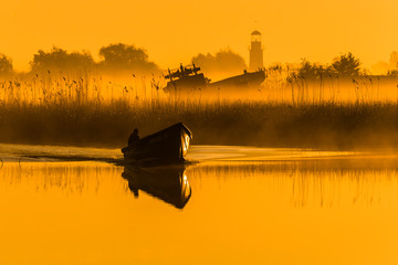 Fisherman is returning to the harbour in Sulina in orange sunraise. Danube delta, Romania