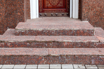 brown wooden entrance door with wood carving pattern on a stone threshold and steps at the granite...