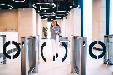 Businesswoman passing through entrance gate in office and talking on phone