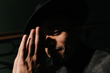 Fototapeta premium Close-up portrait of african man praying in the dark. Indoor shot of joyful male model in black hat.