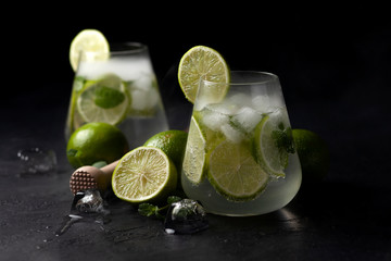 Fototapeta premium two fresh glasses of non-alcoholic mojito, against a dark background, on a black table, summer cocktails with lime and mint