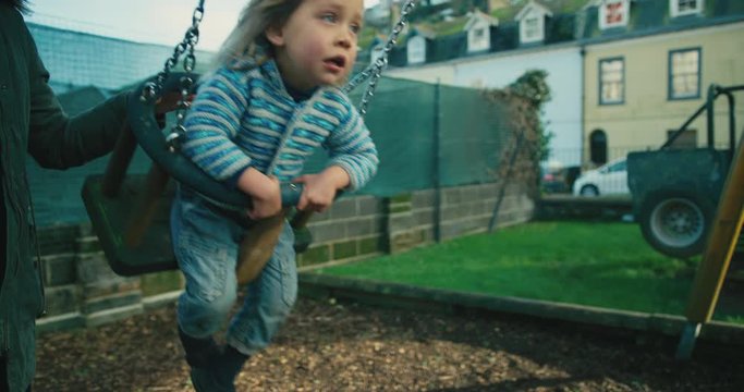 Little preschooler being pushed on swing by his mother