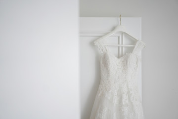 White dress of the bride hangs on a wooden door. Wedding accessories.
