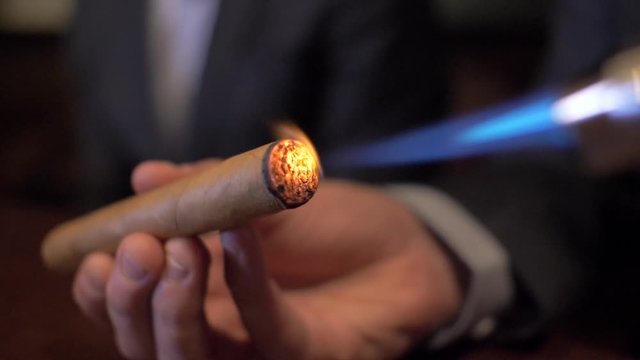 Business man lights cigar with lighter