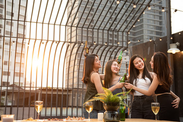 Obraz na płótnie Canvas Group of young beautiful happy asian women holding bottle of beer chat together with friends while celebrating dance party on outdoor rooftop nightclub with copy space for advertising.