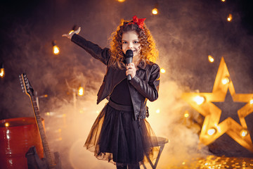 Obraz na płótnie Canvas Beautiful girl with curly hair wearing leather jacket, boots sing into a wireless microphone for karaoke like rock star in recording studio or stage. Smoke on background.