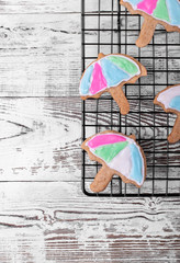 Umbrella shaped shortbread cookies covered with multicolored glazing on the lattice on the white wooden table. Top view