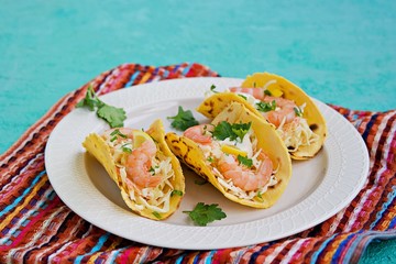 Snack, tacos with coleslaw salad, shrimp and corn tortilla sauce on a light clay plate on a turquoise concrete background. Mexican cuisine.