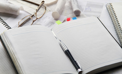 Notebook, pen, glasses, financial documents on the table. Light background.