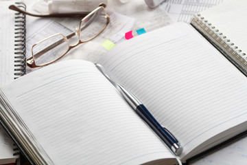 Notebook, pen, glasses, financial documents on the table. Light background.