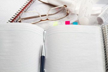 Notebook, pen, glasses, financial documents on the table. Light background.