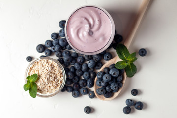 fresh blueberry yogurt in a glass on a white table, cereals and berries, top view