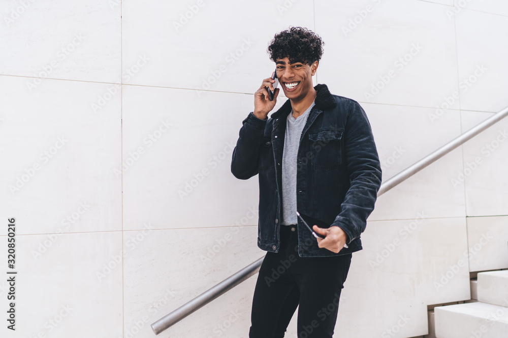 Poster half length portrait of cheerful latino hipster guy smiling at camera while discussing time of meeti