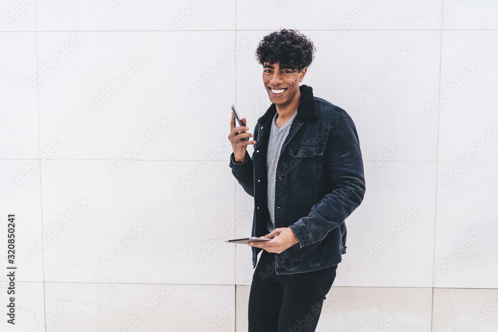 Poster half length portrait of cheerful hipster guy calling via cellphone gadget while standing at copy spa