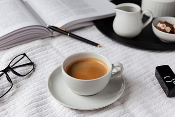Black&white mood. Cup of espresso on a white plaid with a book, glasses and pen. Milk and chocolate on a black tray
