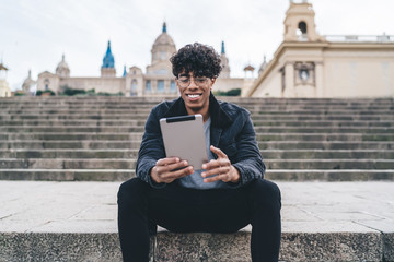 Obraz premium Cheerful African American man sitting on stairs and using tablet