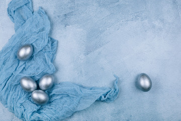 Top view of silver grey painted Easter eggs on napkin on textured blue background. Happy Easter...