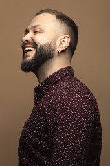 Fabulous at any age concept. Profile portrait of laughing 40-year-old man standing over beige background. Modern haircut. Hipster style. Close up. Studio shot