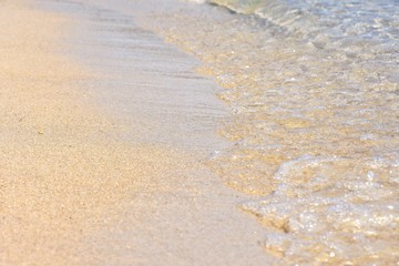 Transparent sea waves with white foam and clean yellow sand. Summer background.  Sea coast with a beautiful soft wave. blue sea wave with white foam on a clean sandy shore, selective focus. 