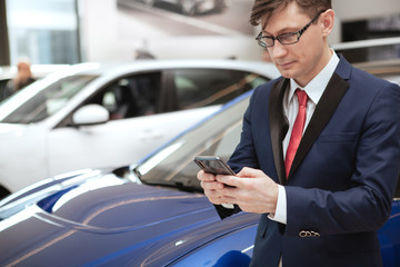 Cropped shot of a mature businesmman using his smart phone while buying car at dealership salon