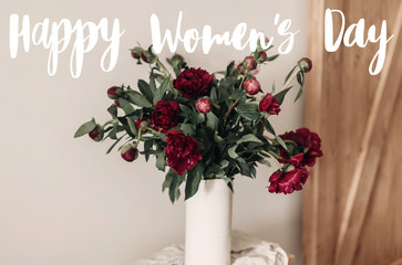 Happy women's day text on stylish peony bouquet in white vase on rustic wooden background. Red and pink peonies rural still life. Greeting card