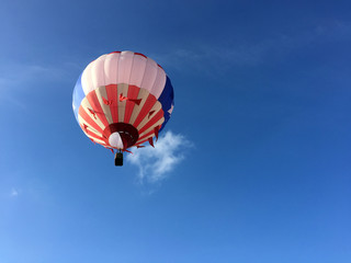 Fototapeta premium single red, white and blue hot air balloon floating up into blue sky, close