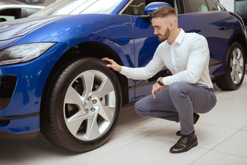 Fototapeta na wymiar Full length shot of a handsome elegant man examining wheels and tires of a car he is buying at the dealership