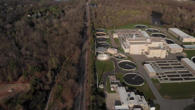 Industrial Water Treatment Plant Facility Near River and Woods Drone Aerial Flyover in Spring